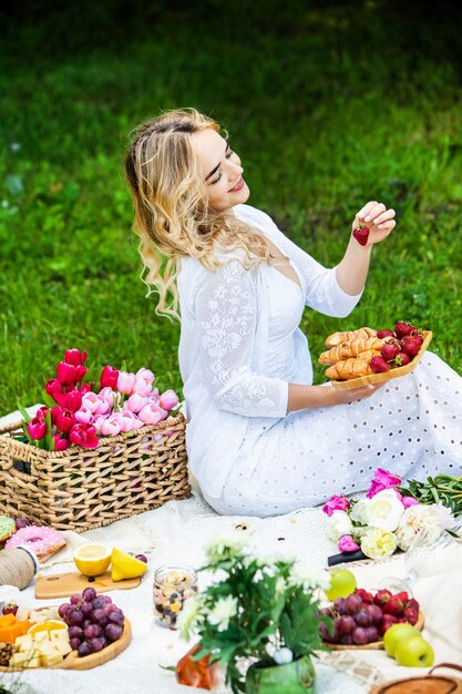 Mooie vrouw rustend in het park zittend op een picknickdeken met fruit en wijn