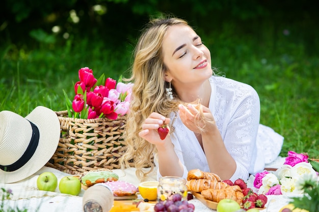 Mooie vrouw rustend in het park zittend op een picknickdeken met fruit en wijn