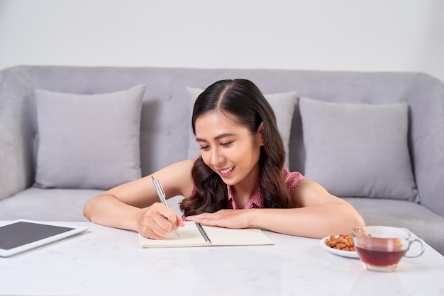 Mooie vrouw thuis schrijven en werken met dagboek en digitale tablet.