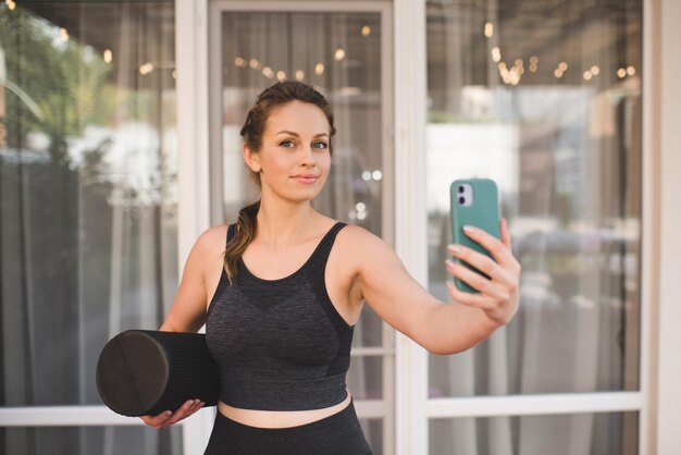 Mooie vrouw van 25-30 jaar oud bereidt zich voor op oefening thuis en maakt selfie met slimme telefoon binnen. Camera kijken. Gezonde levensstijl.