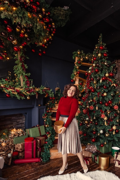 Mooie vrouw van 35 jaar oud met een cadeau in haar handen thuis bij de kerstboom