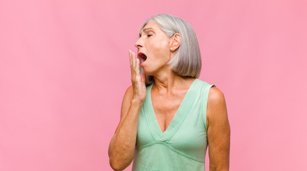 Mooie vrouw van middelbare leeftijd die er gelukkig, zelfverzekerd en betrouwbaar uitziet, glimlachend en een overwinningsteken toont, met een positieve houding