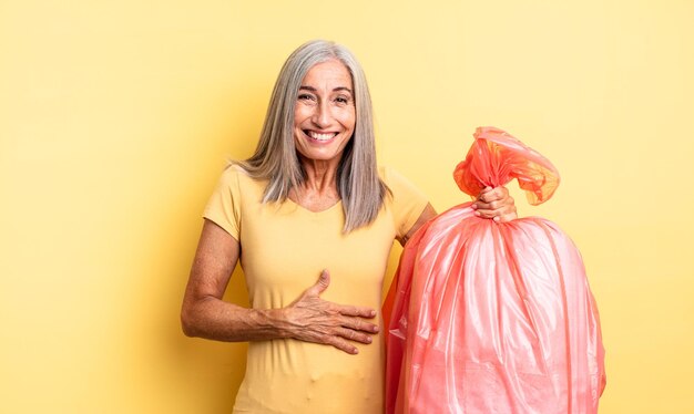 Mooie vrouw van middelbare leeftijd die hardop lacht om een of andere hilarische grap. plastic vuilniszak