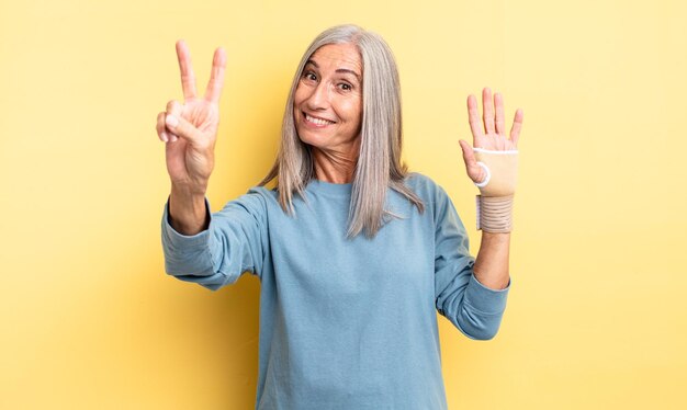 Mooie vrouw van middelbare leeftijd die lacht en er gelukkig uitziet, gebarend naar overwinning of vrede. handverband concept