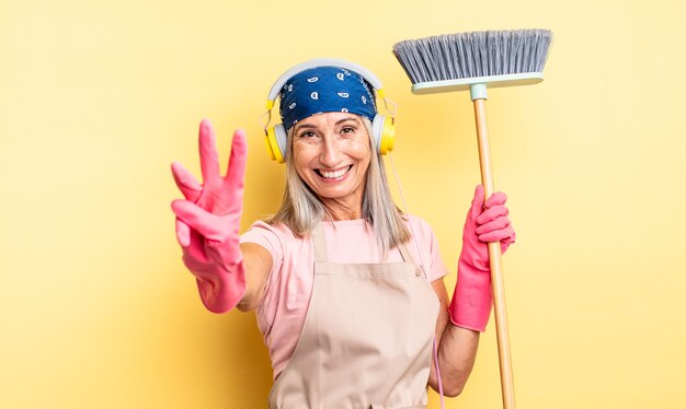 Mooie vrouw van middelbare leeftijd die lacht en er vriendelijk uitziet, met nummer drie. huishoud- en bezemconcept