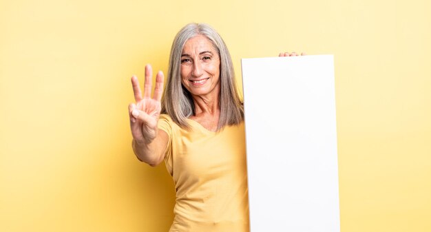 Mooie vrouw van middelbare leeftijd die lacht en er vriendelijk uitziet, met nummer drie. leeg canvasconcept