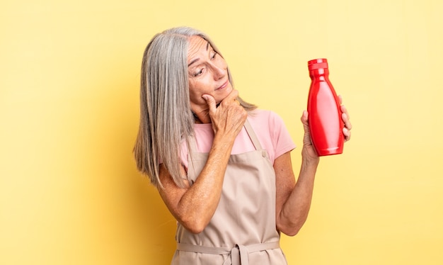 Mooie vrouw van middelbare leeftijd die lacht met een gelukkige, zelfverzekerde uitdrukking met de hand op de kin. ketchup-concept