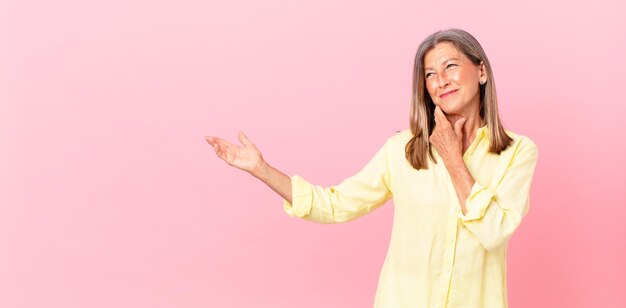 Mooie vrouw van middelbare leeftijd die lacht met een gelukkige, zelfverzekerde uitdrukking met de hand op de kin