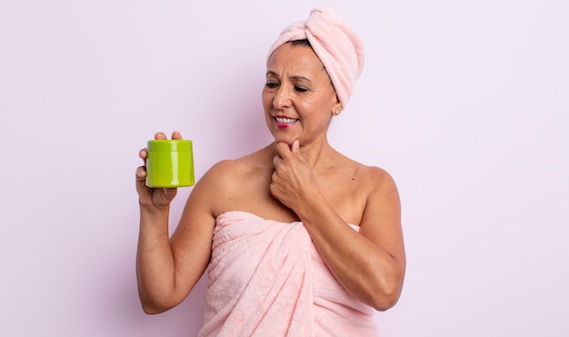 Mooie vrouw van middelbare leeftijd die lacht met een vrolijke, zelfverzekerde uitdrukking met de hand op de kin. douche- en haarproductconcept