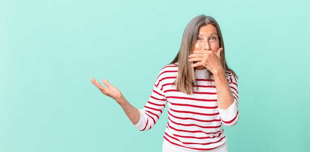 Mooie vrouw van middelbare leeftijd die mond bedekt met handen met een geschokte