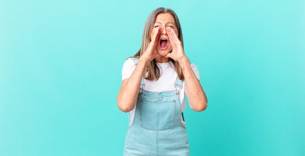 Mooie vrouw van middelbare leeftijd die zich gelukkig voelt en een grote schreeuw geeft met de handen naast de mond