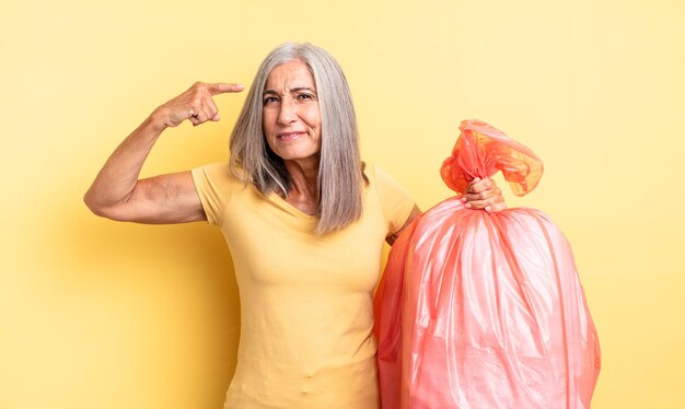 Mooie vrouw van middelbare leeftijd die zich verward en verbaasd voelt en laat zien dat je gek bent. plastic vuilniszak