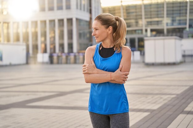 Mooie vrouw van middelbare leeftijd in sportkleding die opzij kijkt terwijl ze buiten staat, klaar voor training