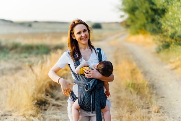 Mooie vrouw van middelbare leeftijd jonge moeder blij met haar 1-jarige zoon terwijl moeder door het veld loopt. concept van haven, borstvoeding, respectvol moederschap