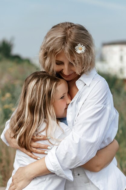 Foto mooie vrouw van middelbare leeftijd omhelst haar dochtertje in de natuur, liefde familie moederschap