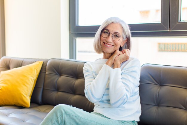 Mooie vrouw van middelbare leeftijd verliefd voelen en er schattig, schattig en gelukkig uitzien, romantisch glimlachend met de handen naast het gezicht