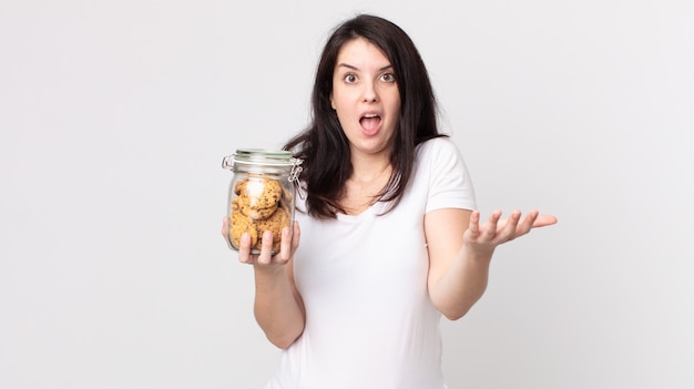 Mooie vrouw verbaasd, geschokt en verbaasd met een ongelooflijke verrassing en met een glazen fles met koekjes