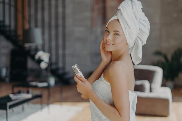 Mooie vrouw verwent huid houdt lotion handdoek binnenlands interieur Schoonheidsverzorging