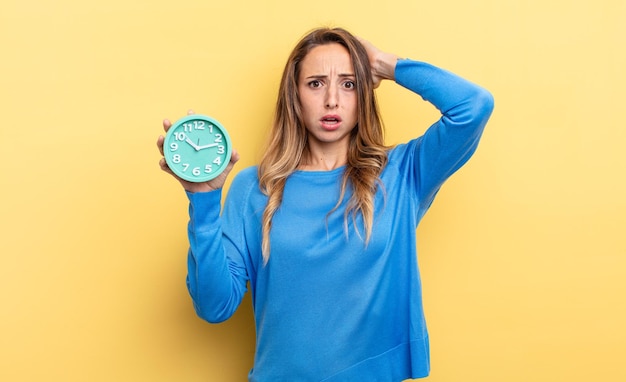 Mooie vrouw voelt zich gestrest, angstig of bang met haar handen op het hoofd en houdt een wekker vast