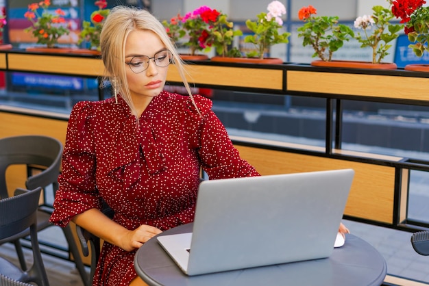 Mooie vrouw werkt op een laptop in een koffieshop en gebruikt een mobiele telefoon in een rood