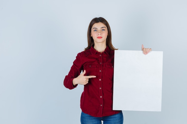 Mooie vrouw wijzend op een leeg bord in bordeauxrode blouse en er zelfverzekerd uitzien