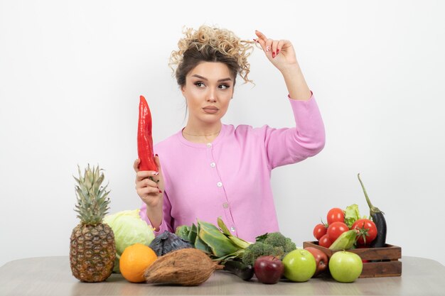 Mooie vrouw zittend aan tafel en rode chili peper te houden.