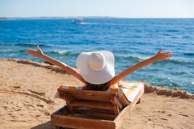 Mooie vrouw zonnebaden op een strand in tropisch reisresort, genietend van zomervakanties die haar handen opsteken.