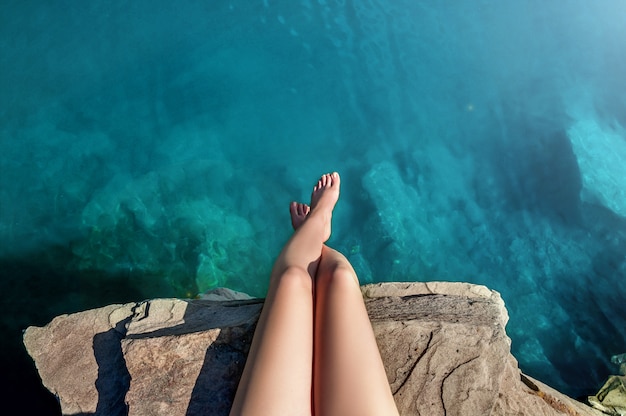 Mooie vrouwelijke benen in Lake Water. Jonge vrouw zittend op steen op het meer. Zomertijd. Reizen concept