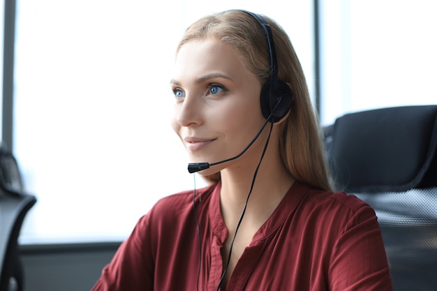 Mooie vrouwelijke callcentermedewerker in koptelefoon werkt op modern kantoor.