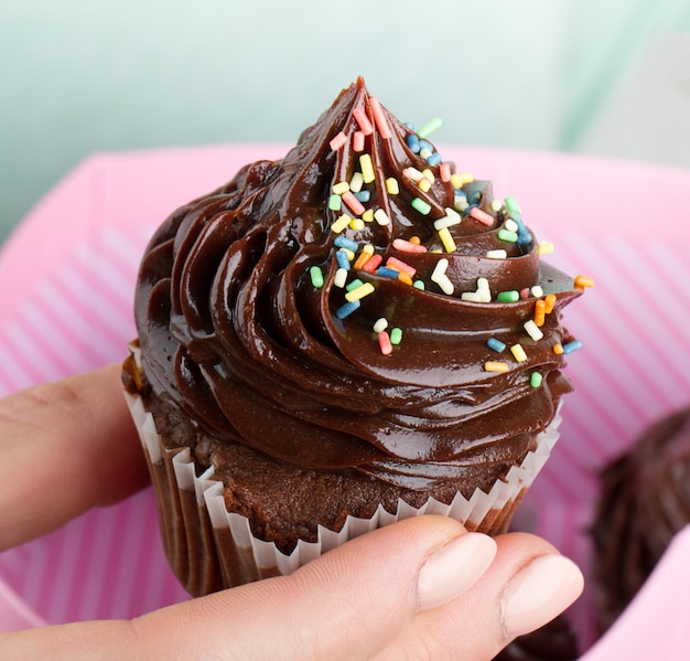 Mooie vrouwelijke hand die smakelijke smakelijke chocolade cupcake houdt. roze gift box. detailopname.