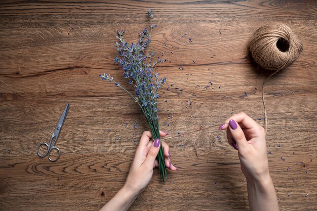 Mooie vrouwelijke handen binden bosje droge lavendel op de achtergrond van eiken tafelblad uitzicht