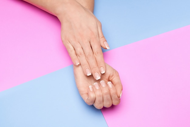 Mooie vrouwelijke handen met Franse manicure over kleurrijke papieren oppervlak