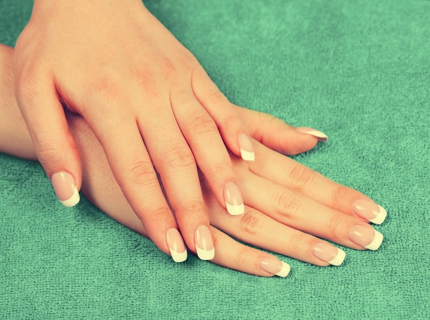 Mooie vrouwelijke handen met french manicure op groene handdoek