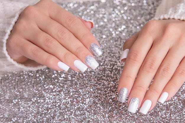 Mooie vrouwelijke handen met romantische manicure nagels, witte gellak met zilveren glitter