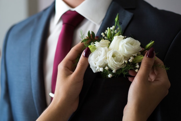 Mooie vrouwelijke handen passen de corsages op de jas aan. Bruid die de corsages van de mooie bruidegom aanpast