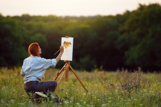 Mooie vrouwelijke kunstenaar schilderen bij zonsondergang in de natuur