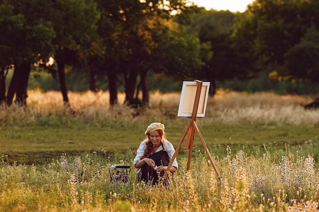 Mooie vrouwelijke kunstenaar schilderen bij zonsondergang in de natuur