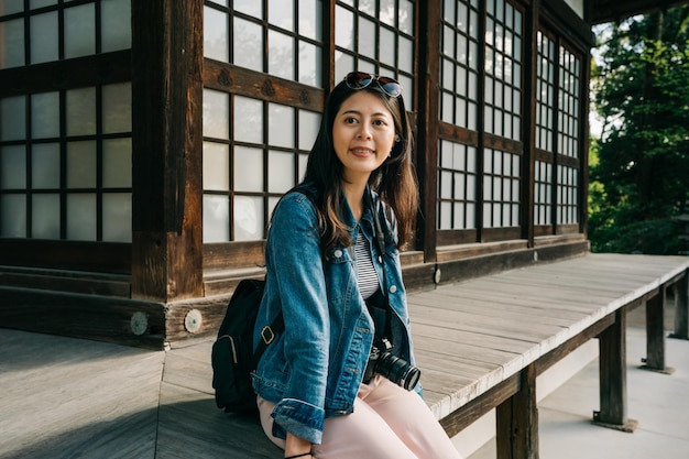 mooie vrouwelijke reiziger ontspannen buiten de houten tempel zitten en vrolijk glimlachen. jong meisje ontspannen in het Japanse gebouw in de voorjaarsvakantie. Reis in Kioto.