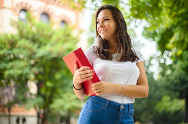 Mooie vrouwelijke student die een boek buiten houdt