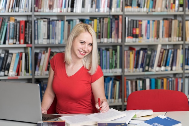 Mooie vrouwelijke student met boeken die in een middelbare schoolbibliotheek werken