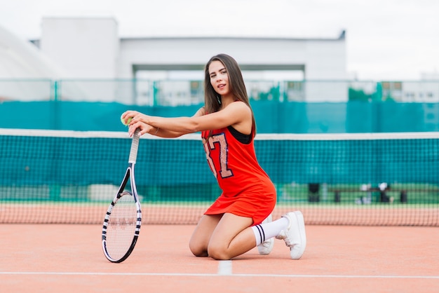 Mooie vrouwelijke tennisspeelster op tennisbaan in rode jurk