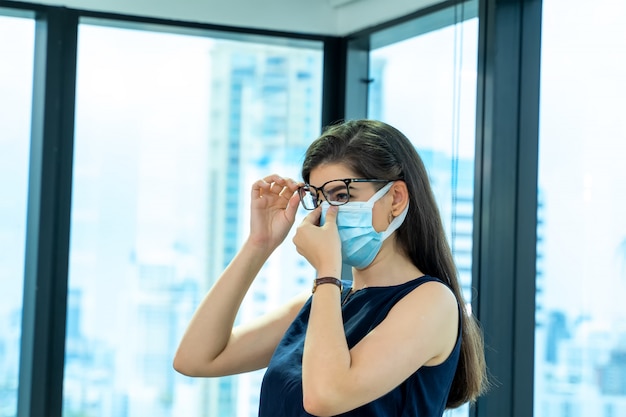 Mooie vrouwelijke werknemer die medisch gezichtsmasker draagt dat alleen werkt vanaf sociaal afstandsbeleid in het bedrijfskantoor tijdens het nieuwe normaal.