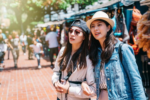 mooie vrouwen die staan te praten over de nieuwe dingen op de Mexicaanse markt in Los Angeles. Vriendschapsconcept met jonge zussen die plezier hebben in de reis van de VS. twee reizigers arm in arm staand.