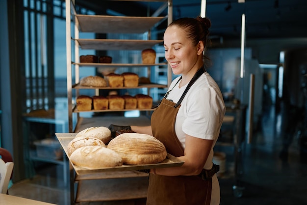 Mooie vrouwenbakker die verscheidenheid van gebakken brood op dienblad houdt