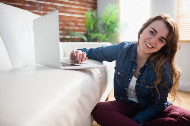 Mooie vrouwenzitting op de vloer die laptop in de woonkamer met behulp van