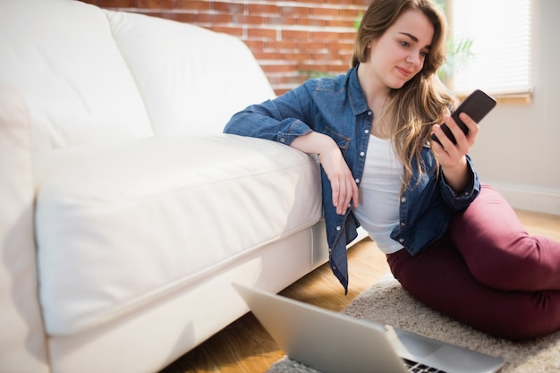 Mooie vrouwenzitting op de vloer die telefoon in de woonkamer met behulp van