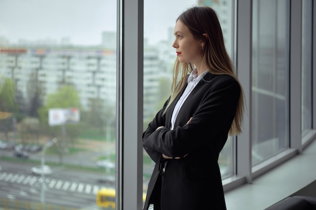 Mooie werknemer van een bouwbedrijf dat door het venster van haar bureau bouwwerf bekijkt