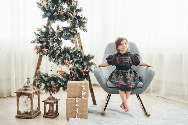 Mooie witte kamer. Kerstmis en vakantie conceptie. Het leuke meisje is zit op de stoel dichtbij ladder met sterren en giftdozen op de vloer wordt verfraaid die