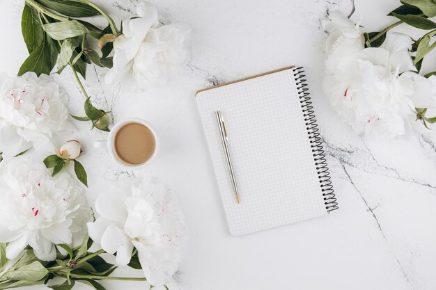 Mooie witte pioenroos bloemen met leeg notitieboekje op witte marmeren stenen achtergrond kopie ruimte voor uw tekst of ontwerp bovenaanzicht plat leggen