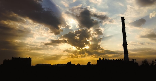 Mooie wolken blokkeren de zon boven de silhouetten van gebouwen en ketelruimleidingen